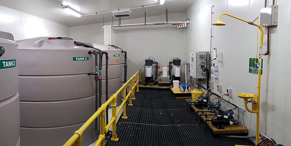 View of large tanks in plant room, looking along platform that has commercial water screen and bag filters