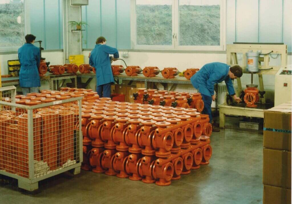 Workers in blue coats working on orange parts of a JUDO product.